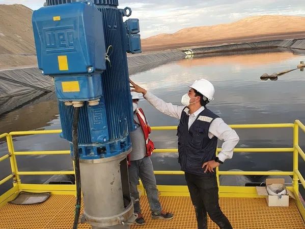 Two workers inspect a large blue industrial pump at a water treatment site.