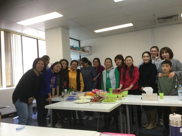 Group of people smiling around a table with food in a bright room.