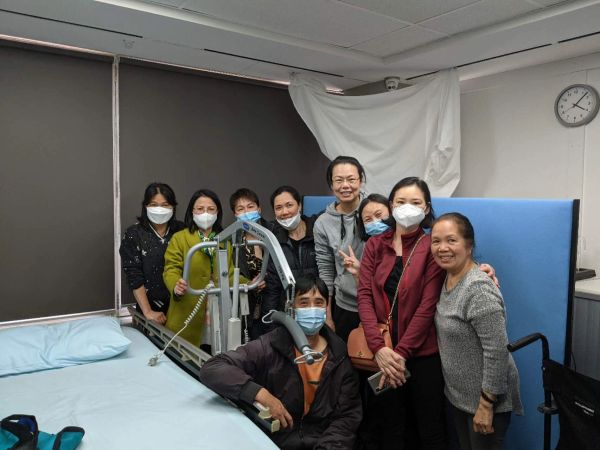 Group of people wearing masks gathered around a hospital bed in a clinical room.