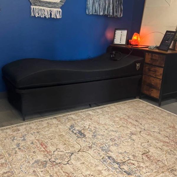 Cozy black chaise lounge against blue wall with wooden cabinet and ornate rug.