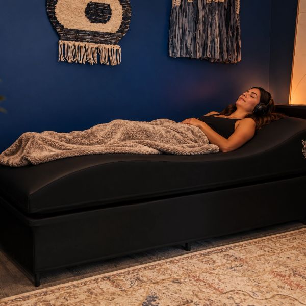Woman relaxing on a black massage bed with a blanket and headphones.