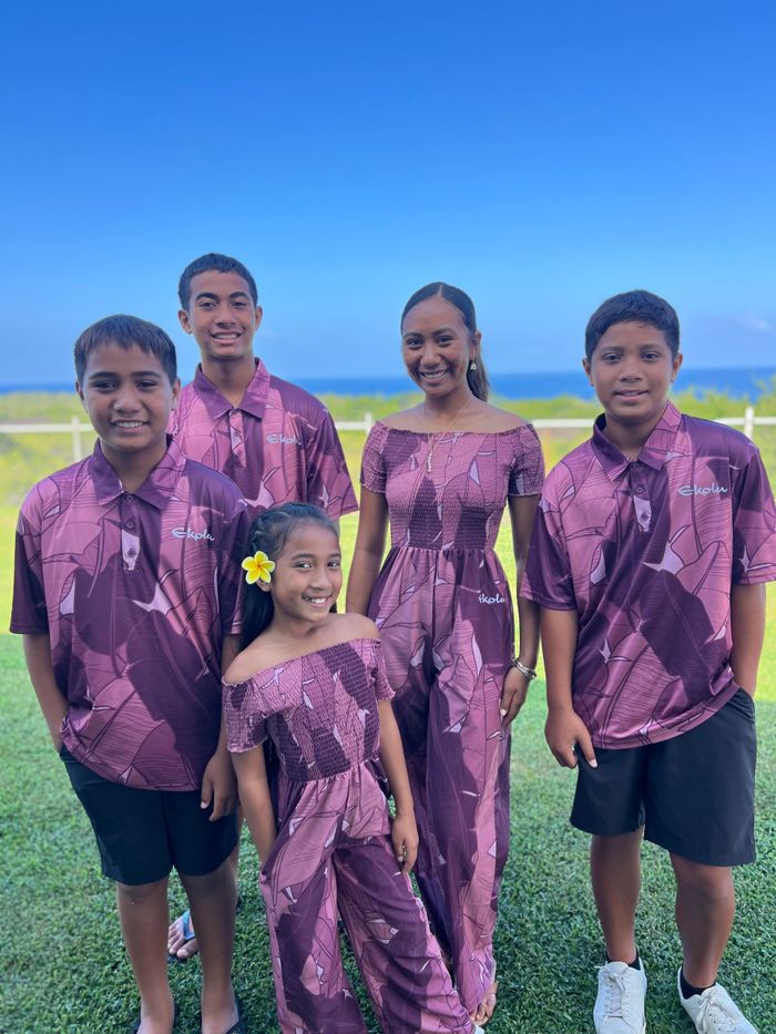 A group of five kids in matching purple outfits smiling outdoors under a clear blue sky.