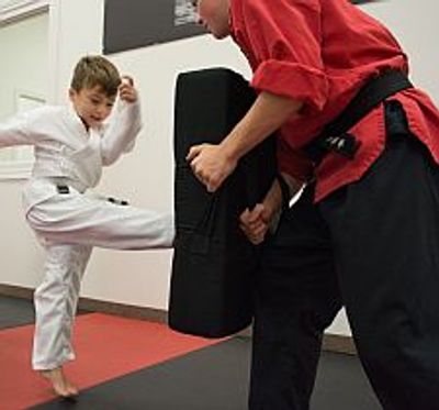 Young boy kicking strike shield held by a man