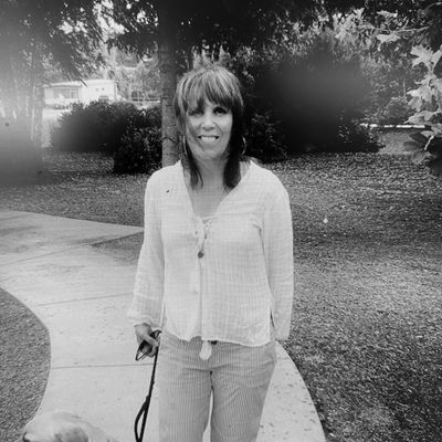 Woman standing on a park path with a dog on a leash.