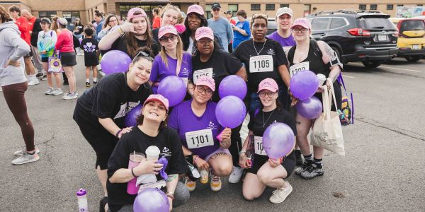 Group of people with purple balloons at an outdoor event.