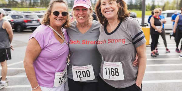 Three women pose with race bibs at outdoor event.