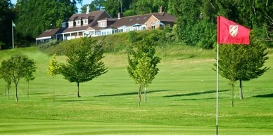 A golf course with a red flag and a clubhouse in the background.