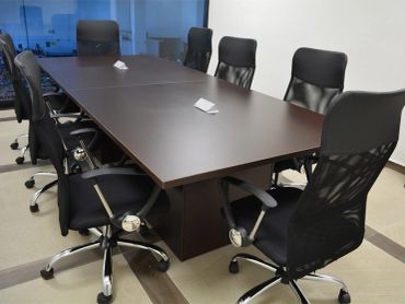 Modern conference room with a long wooden table and black swivel chairs.