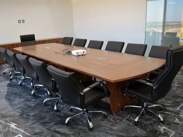 Modern conference room with a large wooden table and black swivel chairs.