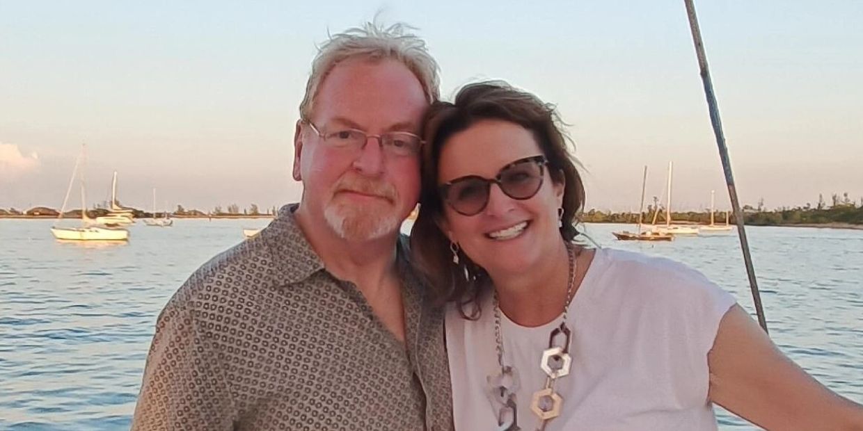 Couple smiling by the water with sailboats in the background.