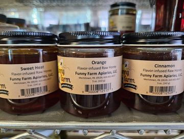 Various jars of flavor-infused raw honey from Funny Farm Apiaries on a store shelf.