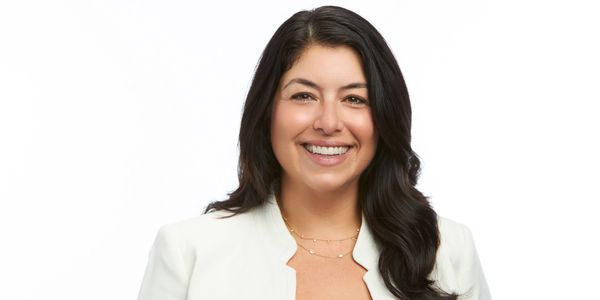 Smiling woman with dark hair in white blazer and black top.