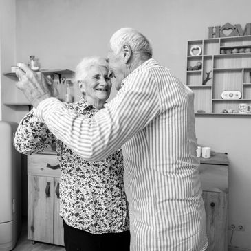An elderly couple dancing in their home, smiling at each other, radiating joy and happiness.