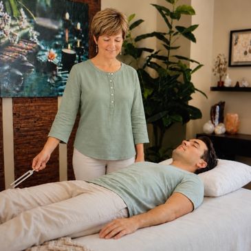 Woman performing healing therapy on man lying down.