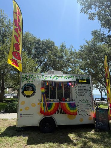 Colorful food truck decorated with rainbow flags in a park.