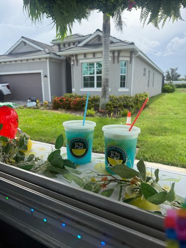 Two blue frozen drinks on a windowsill with a house and lawn in the background.