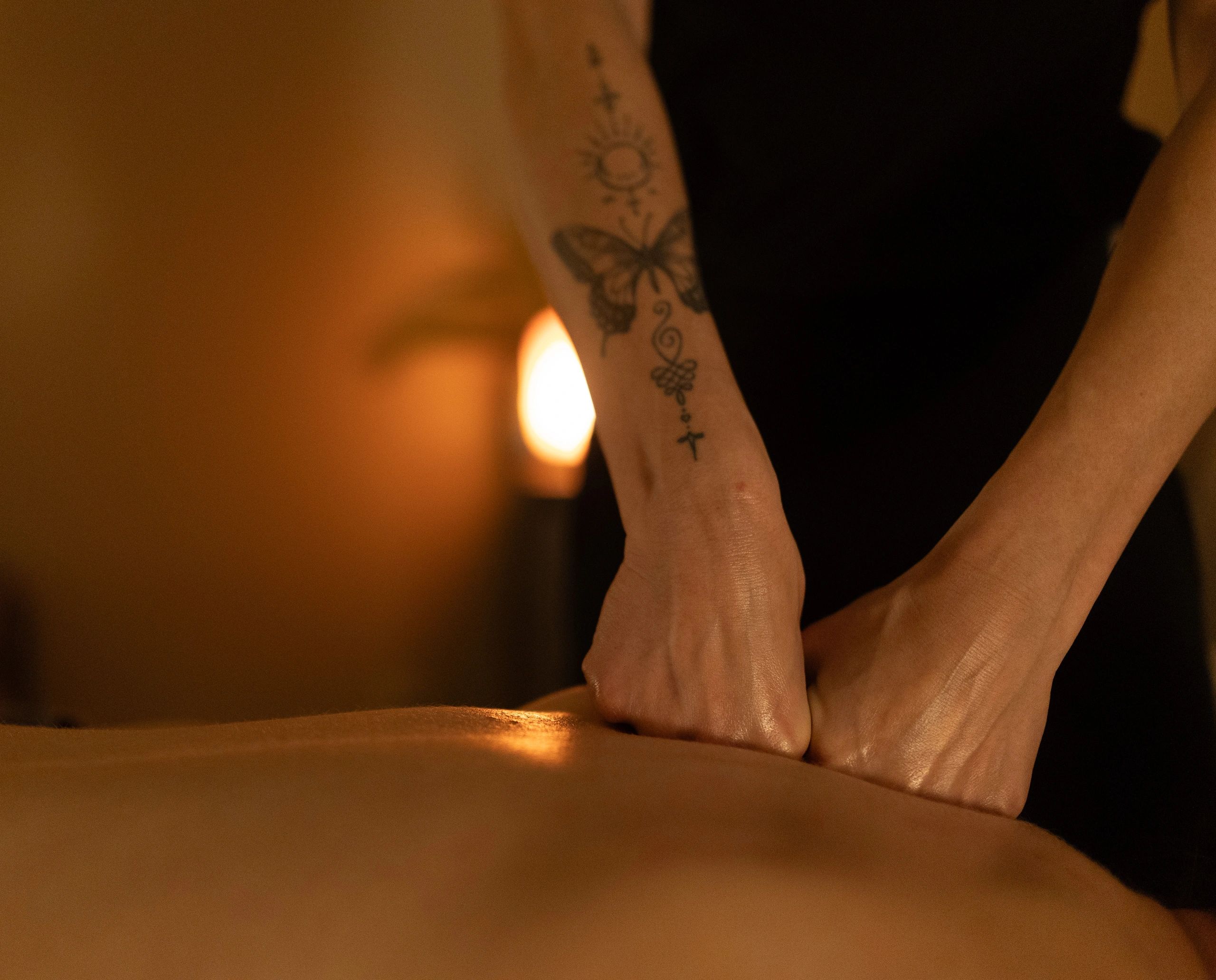 Hands performing a massage with butterfly tattoo visible.