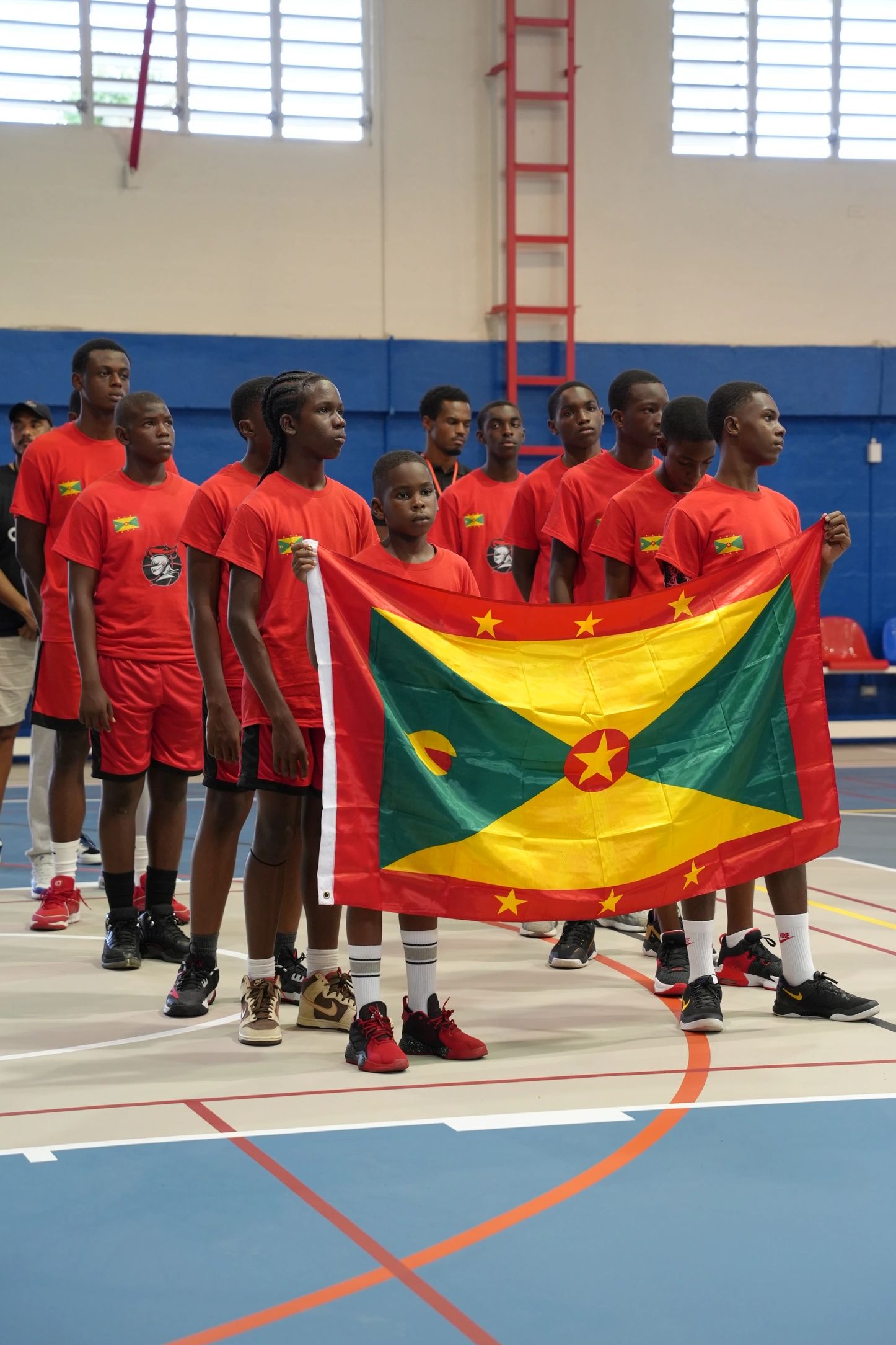 Youth basketball team holding Grenada flag indoors.