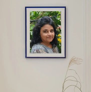 Framed portrait of a woman with dark hair and a gentle smile, surrounded by greenery.