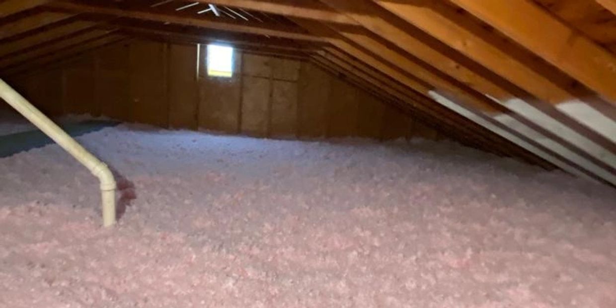 Attic space filled with fluffy pink insulation beneath wooden beams.