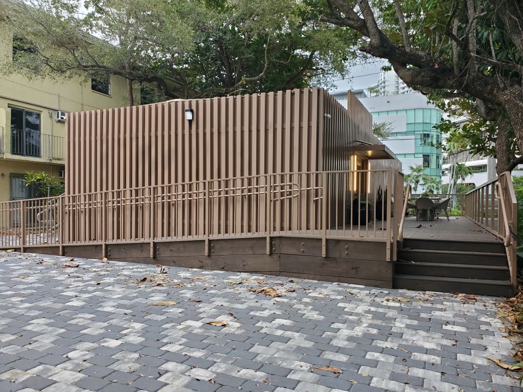 Modern brown building with ramp and stairs surrounded by trees.