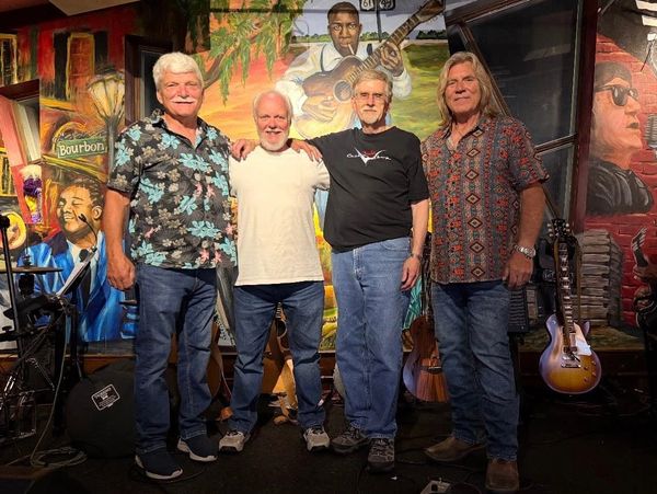 Four men posing on stage with colorful mural background and musical instruments.