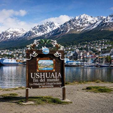 Cartel de bienvenida en Ushuaia con montañas nevadas.