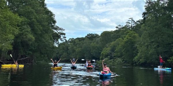 Group kayaking on a calm river surrounded by lush trees.