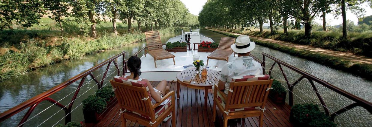 Couple sitting at table on barge cruising treelined canal France.