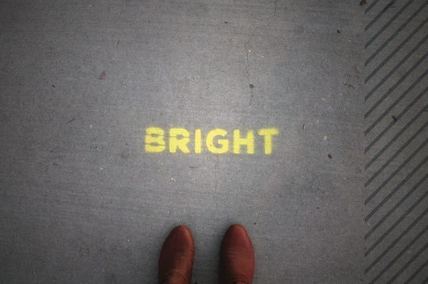 The word 'BRIGHT' stenciled on the ground with brown shoes nearby.