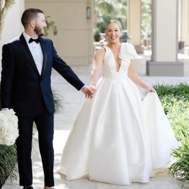 A bride and groom holding hands joyfully outdoors.
