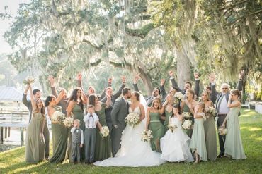 A joyful wedding party celebrating outdoors under large trees.