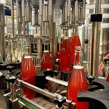 Industrial bottling machine filling glass bottles with red liquid.