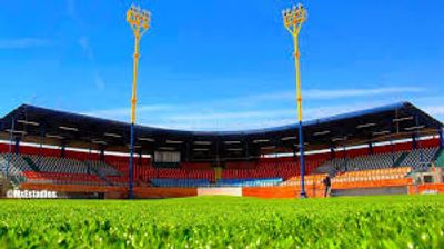 Empty sports stadium with bright green field and floodlights under a clear blue sky.