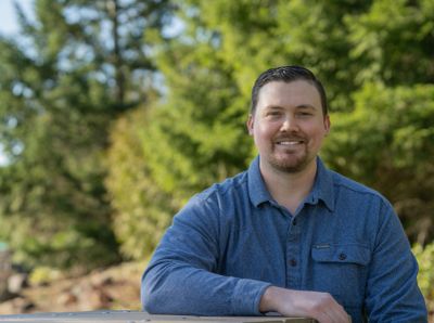Man smiling outdoors with trees in background.