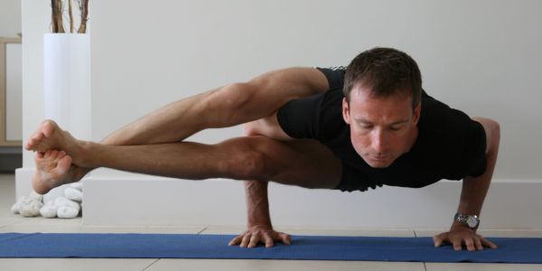 Man performing advanced yoga pose balancing on his hands indoors.