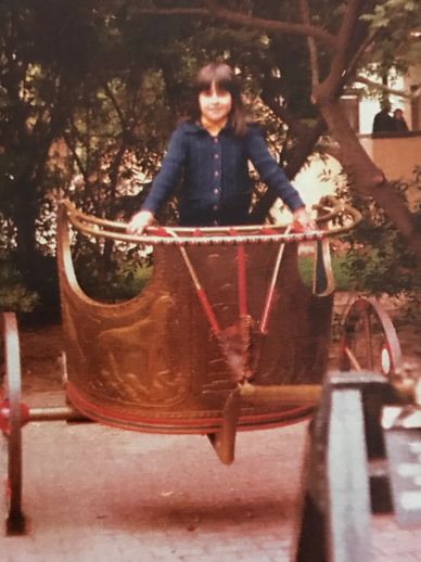 A child standing inside a vintage carousel cup ride outdoors.