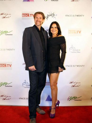 A man and woman posing on a red carpet at an event with a branded backdrop.