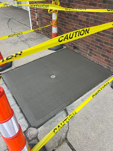 Freshly poured concrete surrounded by caution tape and safety cones.