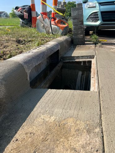 Open storm drain on a roadside under construction with tools and a parked car nearby.