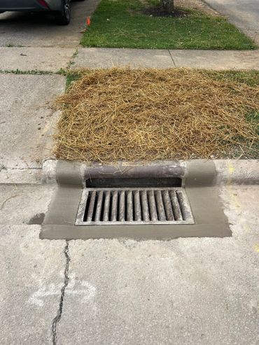 Concrete patching surrounds a storm drain on a city street curb.