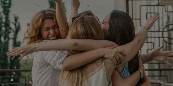 Three women joyfully embracing in a group hug outdoors.