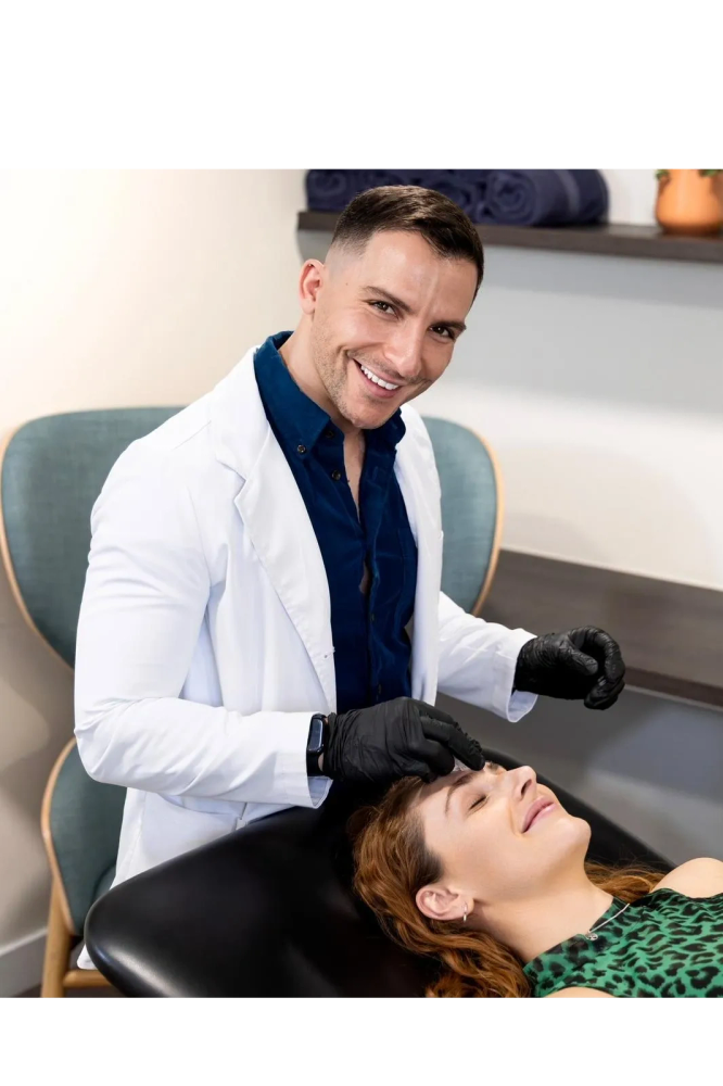 A smiling dermatologist treating a relaxed woman in a clinic.
