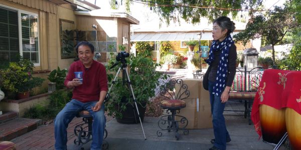 Two people in a garden patio with plants and outdoor furniture.