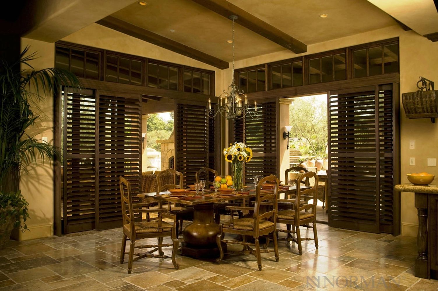 Rustic dining room with wooden furniture and large shuttered windows.