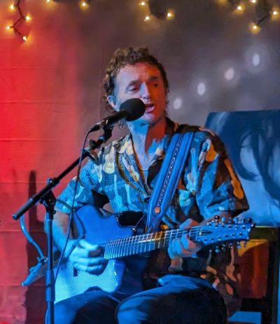 Musician playing guitar and singing on stage with colorful lighting.