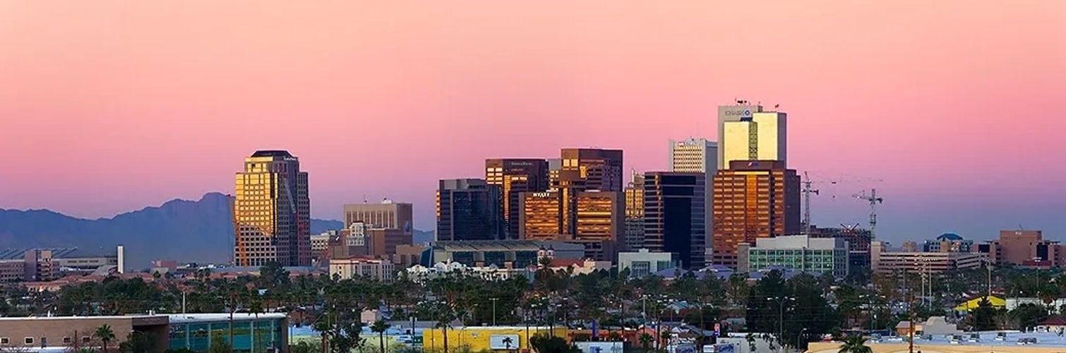 City skyline at sunset with pink sky and mountains in the background.