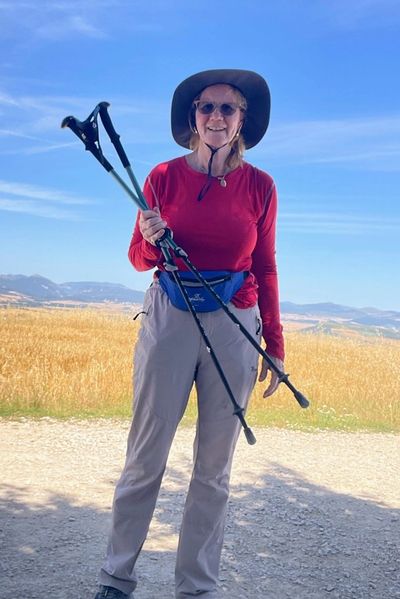 Woman in hiking gear holding trekking poles under a clear blue sky.