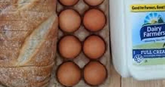 Bread, eggs, and a milk carton on a wooden surface.