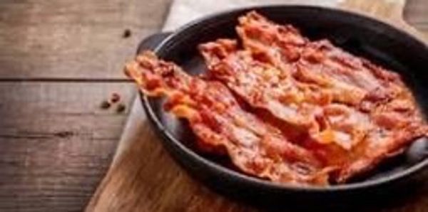 Crispy cooked bacon strips in a black skillet on wooden surface.